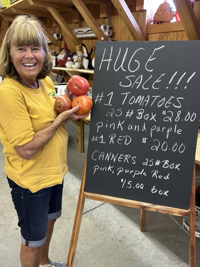Bernie holding tomatoes beside a chalkboard sale sign